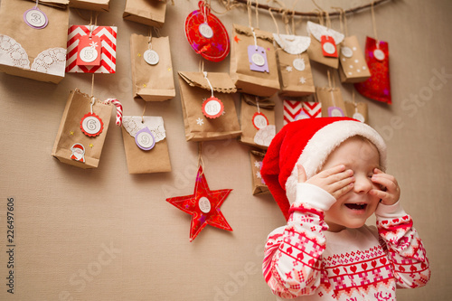 advent calendar for kids. child in a Christmas cap and pajamas happy and playing peek a Boo