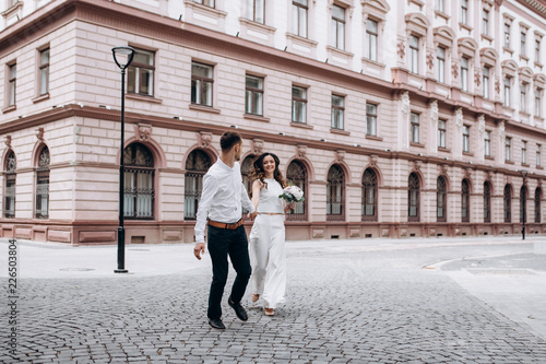 Bride and groom hold each other hands walking along the street in an old European town © kristina_1994