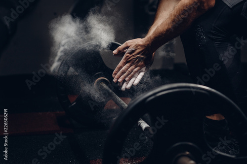 Weightlifter preparing for training workout lifter barbell. Hands in dust and talc. Dark background.