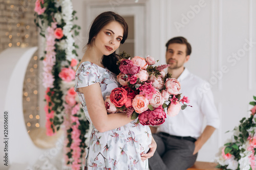 Man looks with love at a pretty pregnant woman standing in bright studio