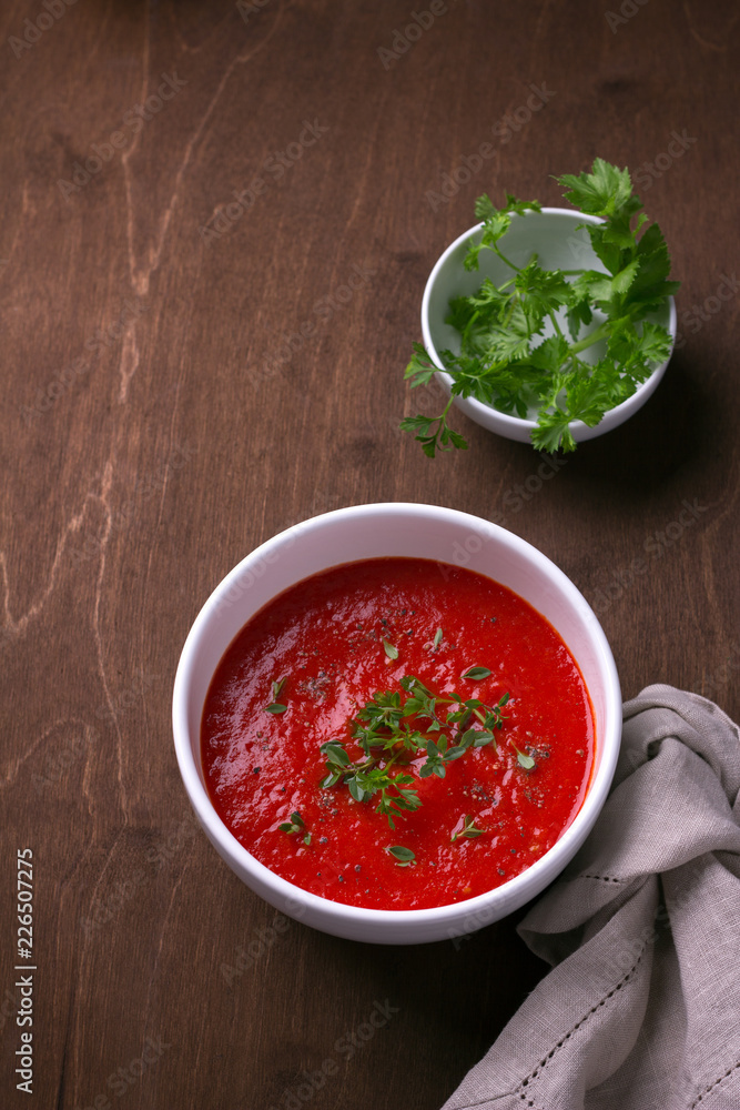 Delicious vegan soup of baked tomatoes and sweet peppers with herbs in a white plate on a wooden background, top view, free space Delicious vegan soup of baked tomatoes and sweet peppers with herbs in a white plate on a wooden background, top view, free space