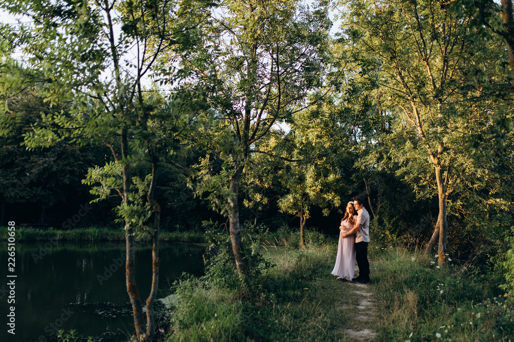 Expecting man and woman walk along the path across the field with sunflowers in beautiful summer evening