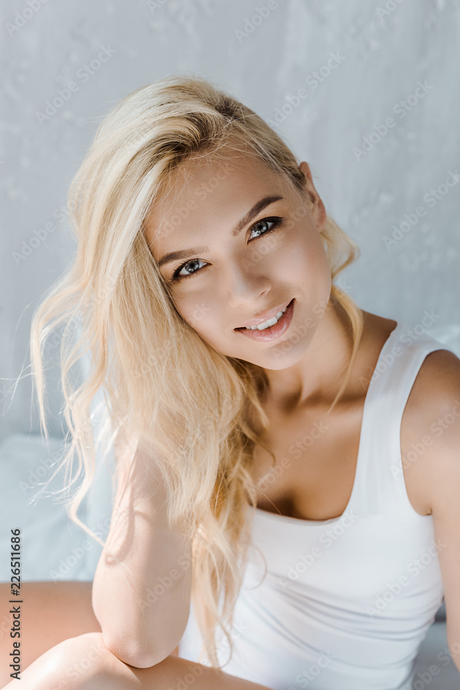 portrait of beautiful young blonde woman in underwear smiling at camera in bedroom