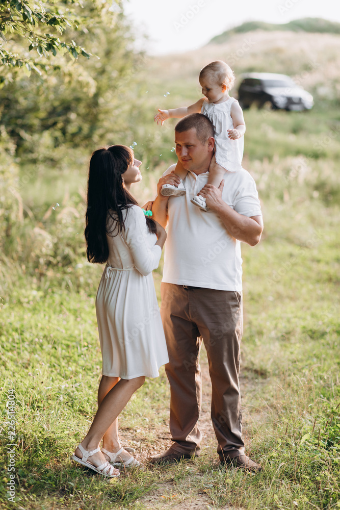 Young parents walk with their lovely little daughter in jeans dress across the field Young parents walk with their lovely little daughter in jeans dress across the field
