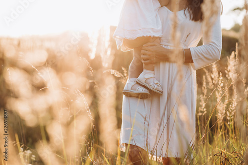 Beautiful portrait of charming mother and lovely little daughter walking across the field in the rays of evening sun