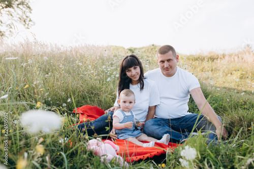 Young mom and dad lie on plaid with their little daughter on a plaid in a green summer field