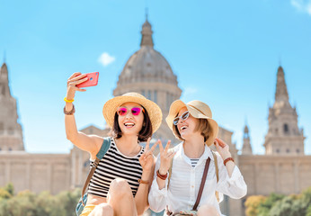Two young happy women tourists friends hugging against the background of the National Museum of Art near the Plaza of Spain and the Montjuic Fountain in Barcelona