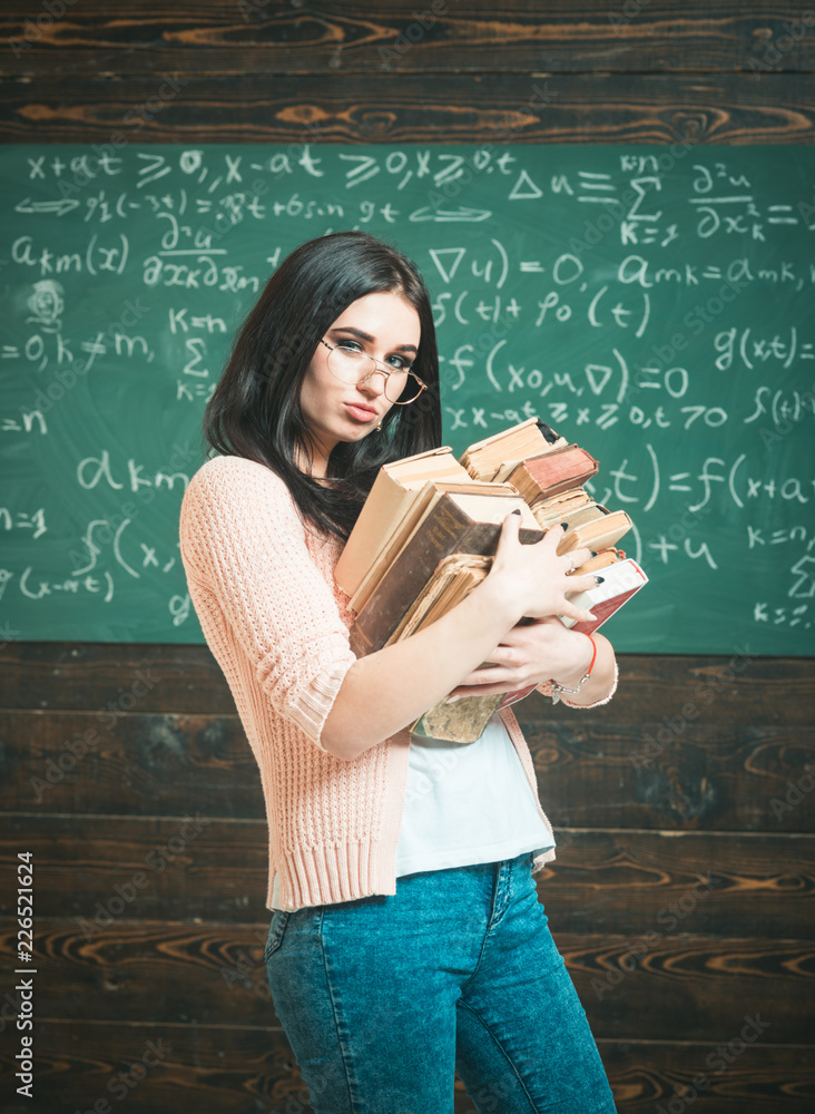 Brunette female student in classroom. Sexy young college girl walking with  two heaps of books Stock Photo | Adobe Stock