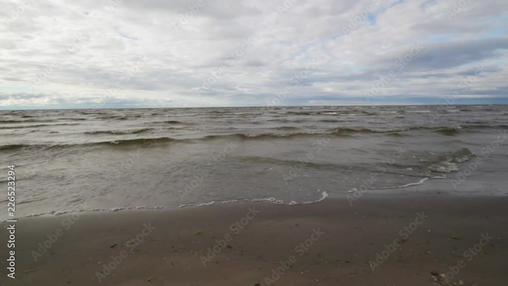 Marvelous scenery of bright blue summer sky covered with clouds and sea underneath with brown waves slowly falling on sand shore on warm windy day. Marvelous scenery of bright blue summer sky covered with clouds and sea underneath with brown waves slowly falling on sand shore on warm windy day.