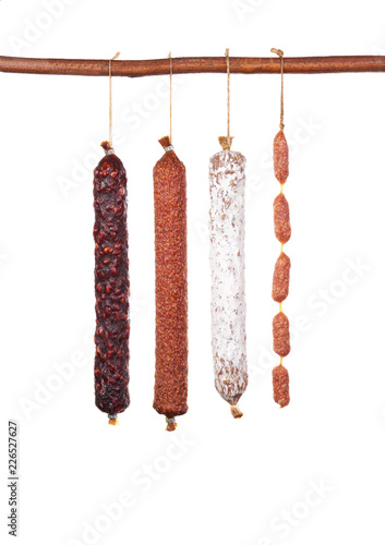 various types of traditional salami hanging on a wooden crossbar isolated on white background