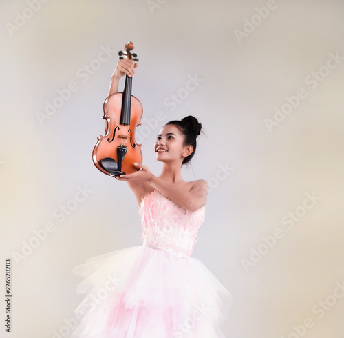 The beauty lady is wearing ballet dress,raising violin up in the air,warm light tone,blurry light design background