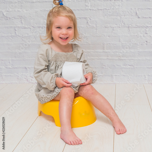 Billede på lærred girl in a dress, a child sitting on a yellow pot with toilet paper in his hands