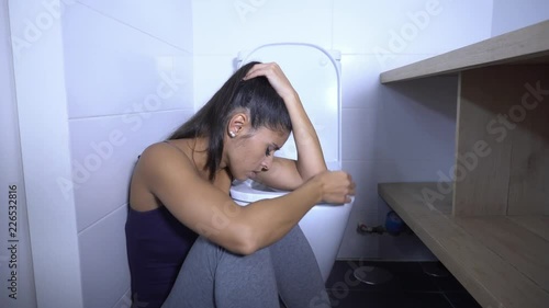 Attractive young and sad bulimic young woman feeling guilty and sick eating while sitting on the floor next to the toilet in eating disorders anorexia and bulimia concept. photo