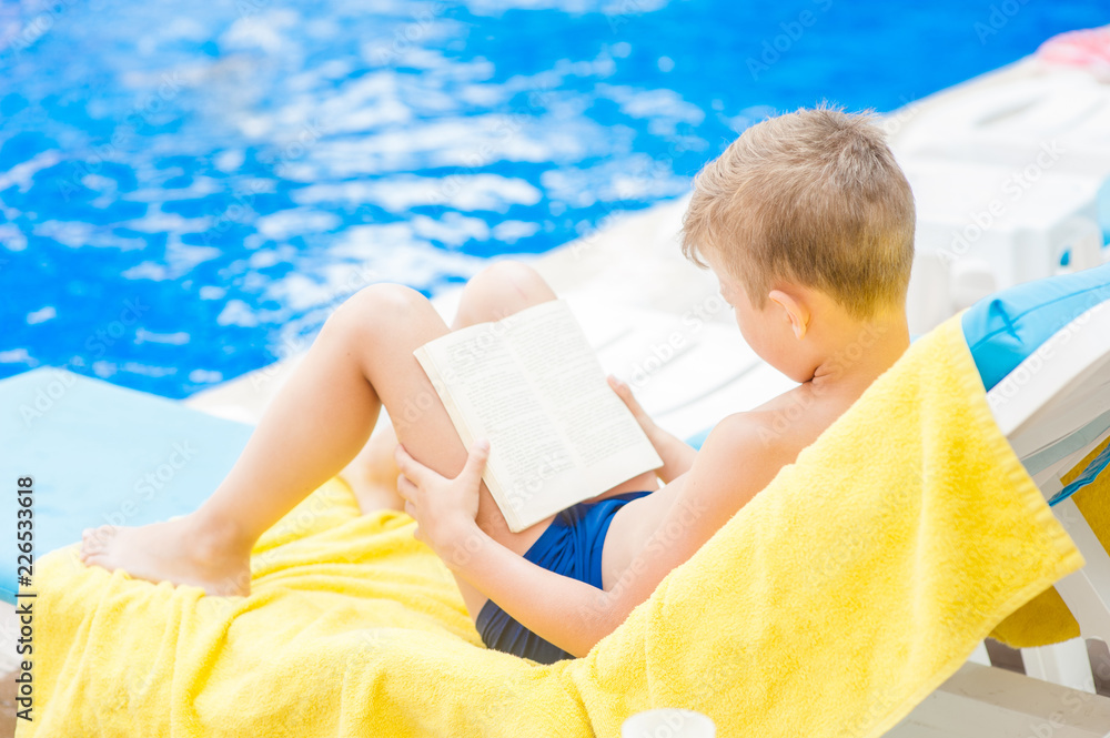 Little boy reading a book by the pool.  Relaxation resting vacations concept. Space for text