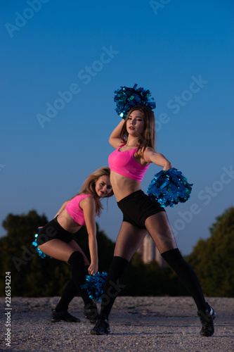 Two girls cheerleaders with pompons dancing outdoors