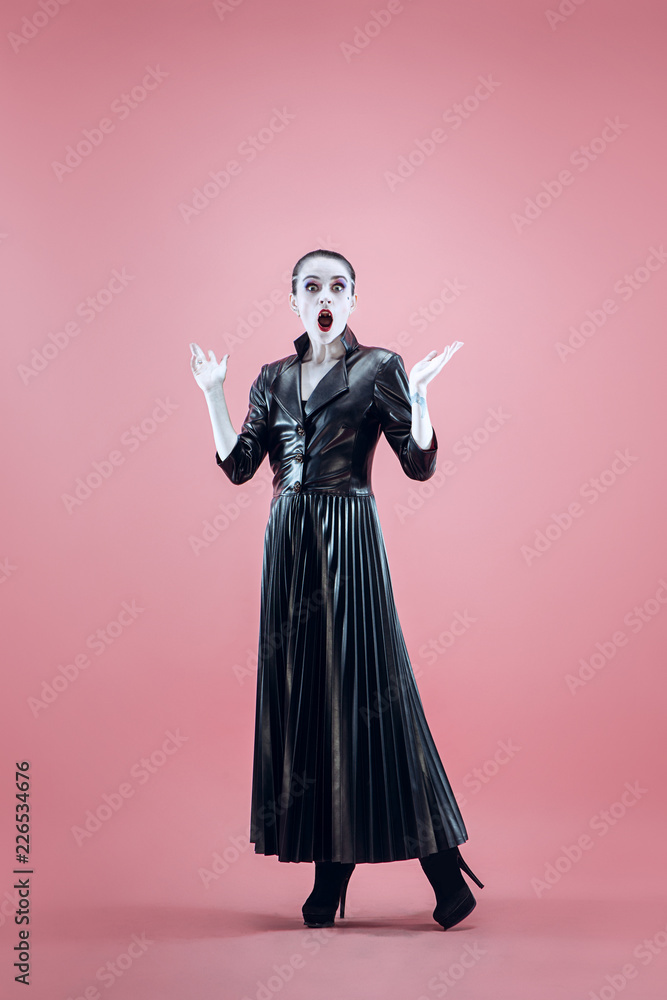 Halloween. Beautiful woman with bright black halloween makeup in a black leather cloak at pink studio Halloween. Beautiful woman with bright black halloween makeup in a black leather cloak at pink studio