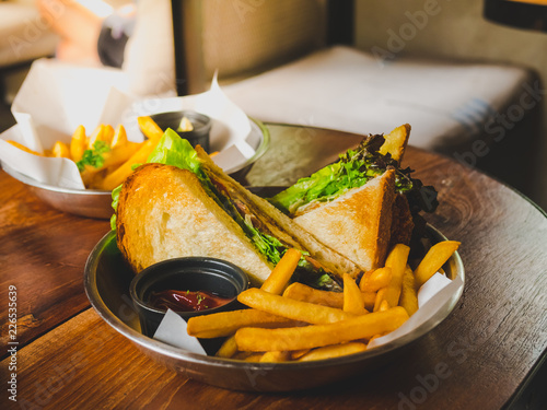 Sandwich with tuna vegetable, tomato, cheese and golden French fries potatoes on wooden table.