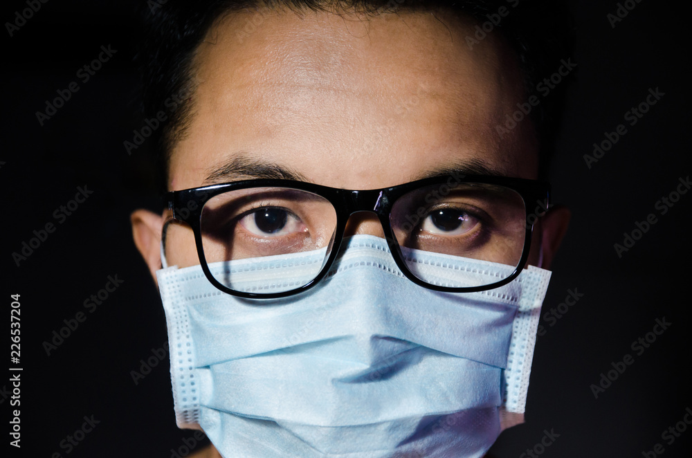close up of young asian man wearing hygienic mask annd glasses with dark blackground close up of young asian man wearing hygienic mask annd glasses with dark blackground
