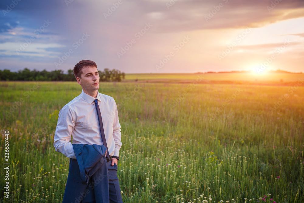 Businessman in elegant suit with his jacket hanging over his shoulder standing in field