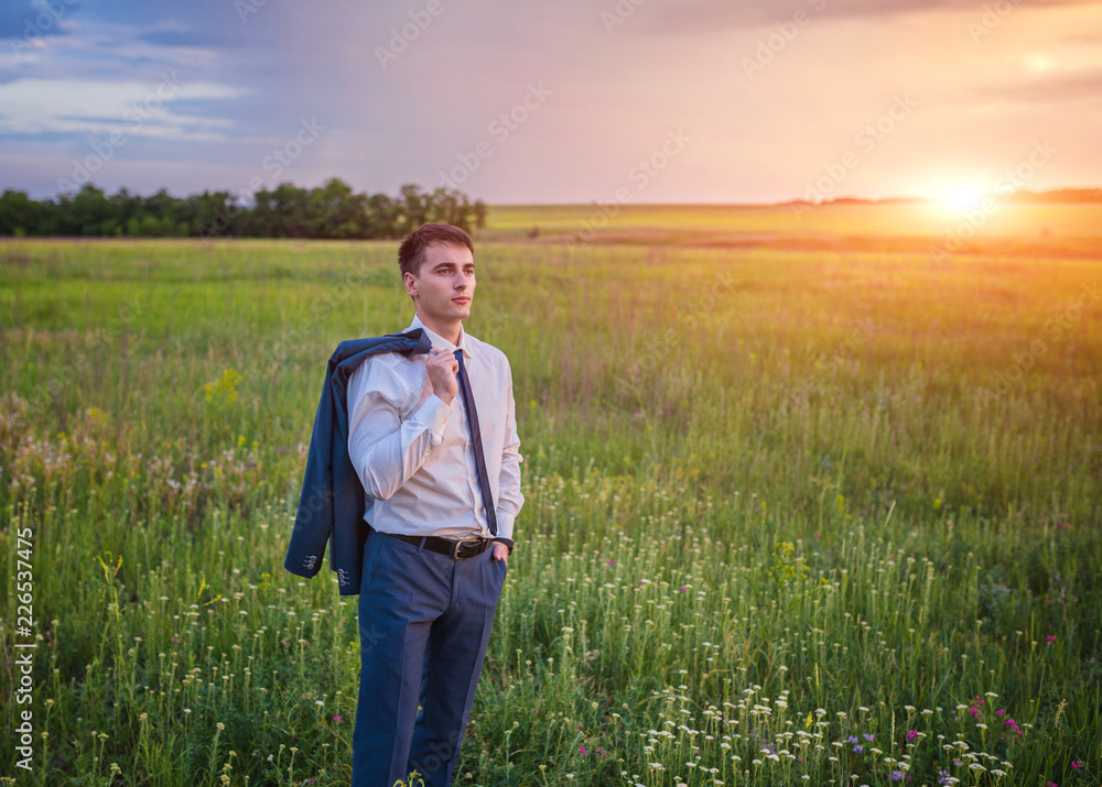 Businessman in elegant suit with his jacket hanging over his shoulder standing in field