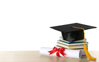 Graduation hat with books and diploma on table against white background