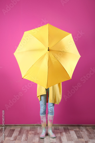 Woman hiding behind yellow umbrella near color wall