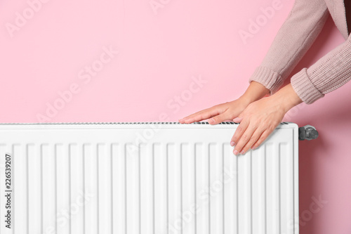 Woman warming hands on heating radiator near color wall