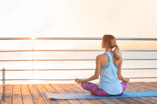 Young woman doing yoga exercises on pier in morning