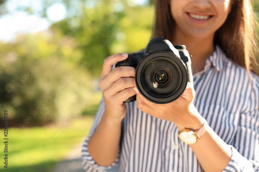 Young female photographer with professional camera in park, closeup. Space for text
