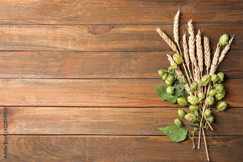 Fresh green hops and wheat spikes on wooden background, top view with space for text. Beer production