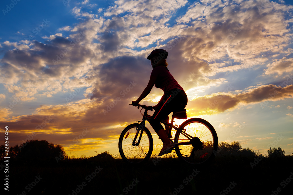 Silhouette of girl cyclist riding against the sunset