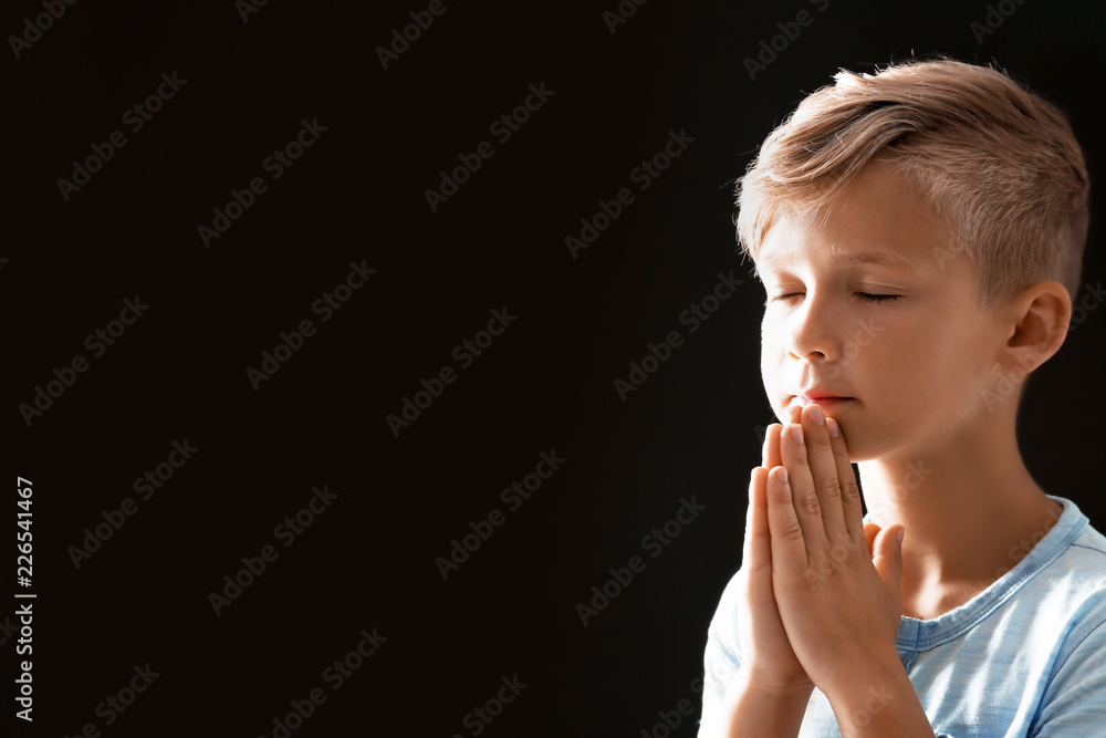 Little boy with hands clasped together for prayer on black background. Space for text