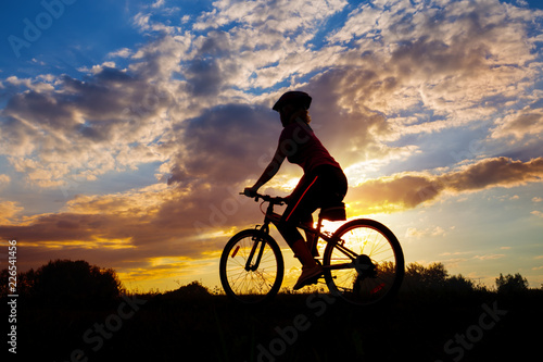 Silhouette of girl cyclist riding against the sunset
