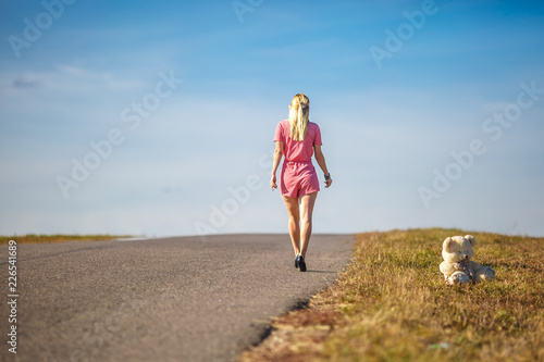 girl in plaid suit leaves on asphalt road from teddy bear. concept of ending childhood