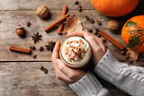 Woman holding glass of tasty pumpkin spice latte on wooden table, flat lay composition