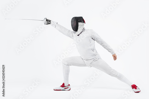 Young fencer athlete wearing mask and white fencing costume. holding the sword. Isolated on white background © Mike Orlov