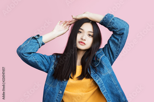 A tranquil female face of Asian appearance on a pink background in a studio with dark hair in a denim jacket. Model snaps are examples of model works and parameters. Stylish and fashionable