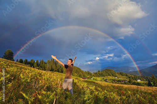 young guy, a tourist, raised his open palms and raised his hands and face upwards, rejoicing in the rainbow