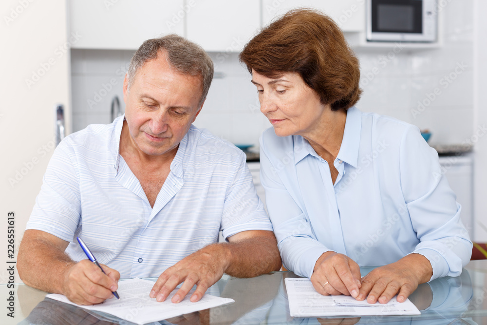 Smiling mature couple  at table in home kitchen filling up documents