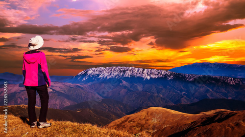 Stunning sunset over the mountains ridge. Woman sitting on a mountain top and looking to the sunset over the mountains in front of her.