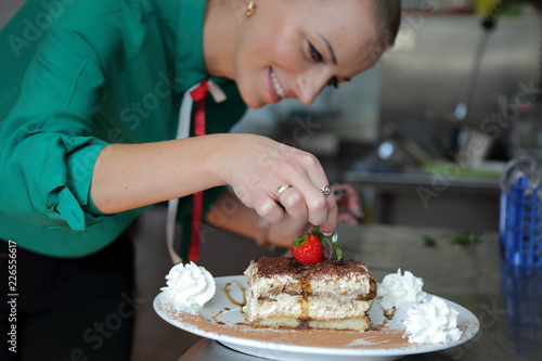 Tiramisu, kelnerka dekoruje ciastko z truskawką listkiem bazyli.