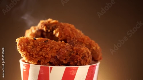 Rotation Bucket full of crispy kentucky fried chicken with smoke on brown background.