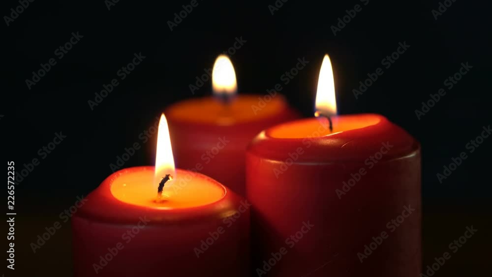 Three thick red Christmas candles burn on a black background Three thick red Christmas candles burn on a black background