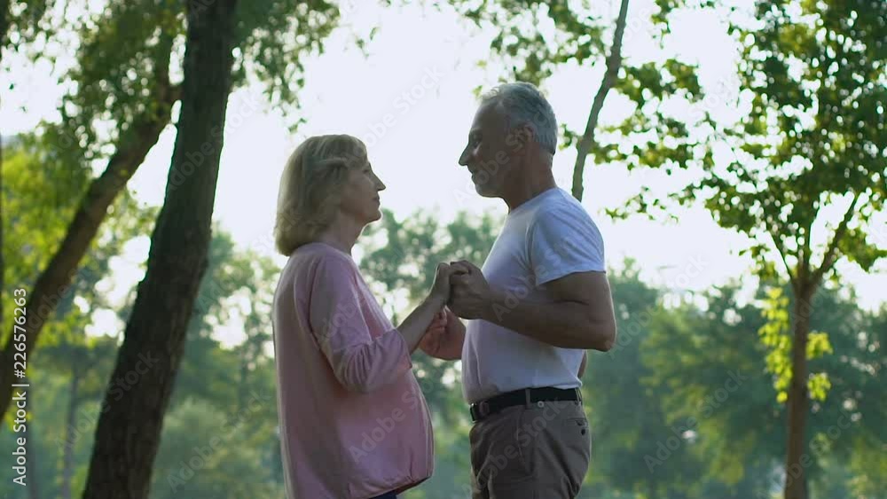 Happy old couple holding hands and dancing in beautiful green park, slow motion
