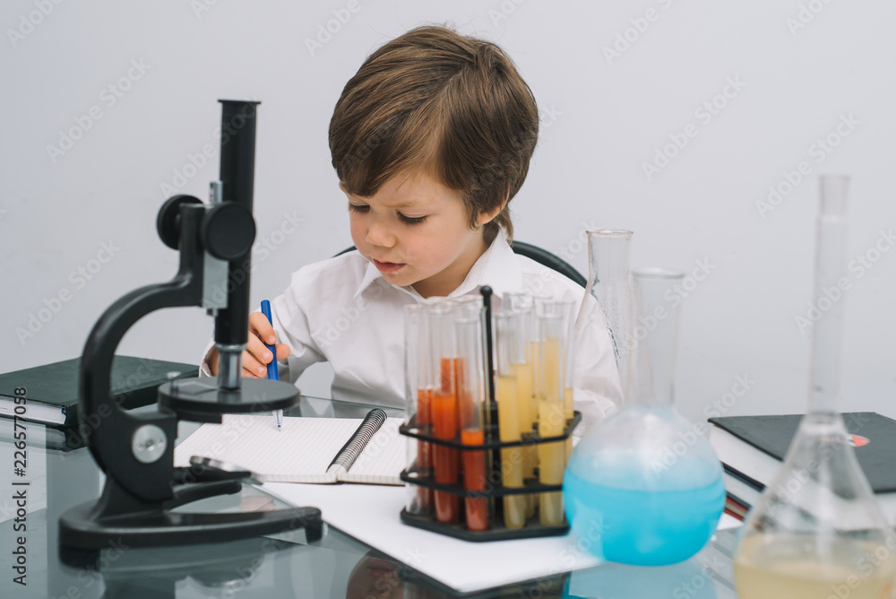 The boy with a microscope and various colorful flasks on a white background. A boy doing experiments in the laboratory. Explosion in the laboratory. Science and education. The boy with a microscope and various colorful flasks on a white background. A boy doing experiments in the laboratory. Explosion in the laboratory. Science and education.