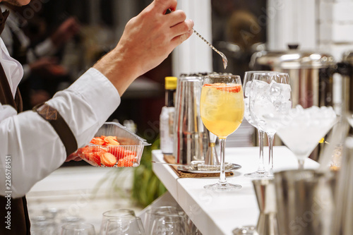 Bartender's hand serving a cocktail. Orange cocktails with fruit slices on the bar counter.