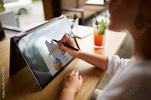 Businesswoman hand pointing with stylus on the chart over convertible laptop screen in tent mode. Woman using 2 in 1 notebook with touchscreen for work on business presentation. Isolated close view. photo