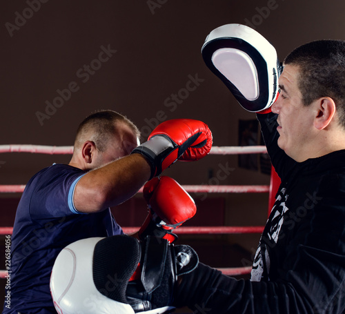 man in gloves boxing with trainer holding focus mitts while standing on ring