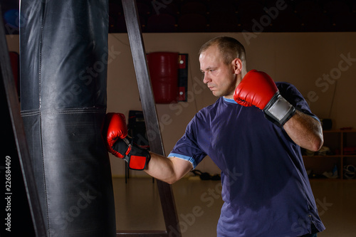 Bilde på lerret novice male boxer training with punching bag on dark background.