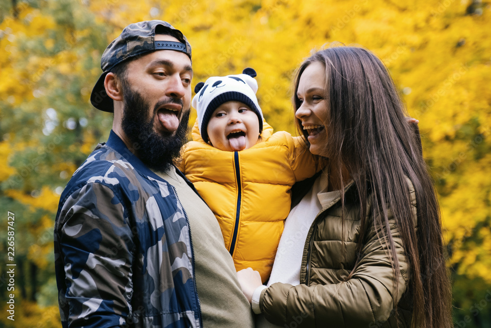 Happy family having fun outdoor. Close up portrait. Father, mother and daughter shows tongue. Autumn walk in the park